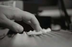 "A black-and-white image showcasing a close-up of a hand adjusting a slider on an audio mixing console, with the text 'Deminiature Pour' in a refined font, emphasizing precision and creativity in sound production."