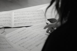 "A black-and-white close-up of Gabrielle Martin's hand marking sheet music, capturing the creative process and meticulous attention to detail in her compositions."