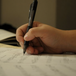 "A close-up of Gabrielle Martin's hand marking sheet music, capturing the creative process and meticulous attention to detail in her compositions."